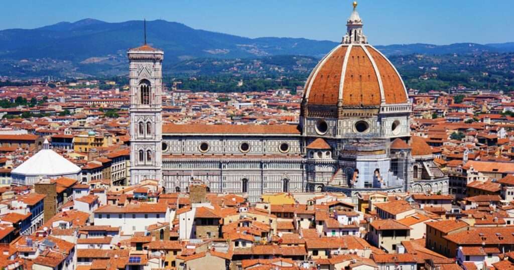 イタリア・ミラノにある世界遺産「サンタ・マリア・デッレ・グラツィエ教会とドメニコ会修道院」の外観。青空の下、赤茶色のレンガ造りの美しいファサードと、ブラマンテ設計による特徴的なルネサンス様式のドーム(クーポラ)が広がっている。